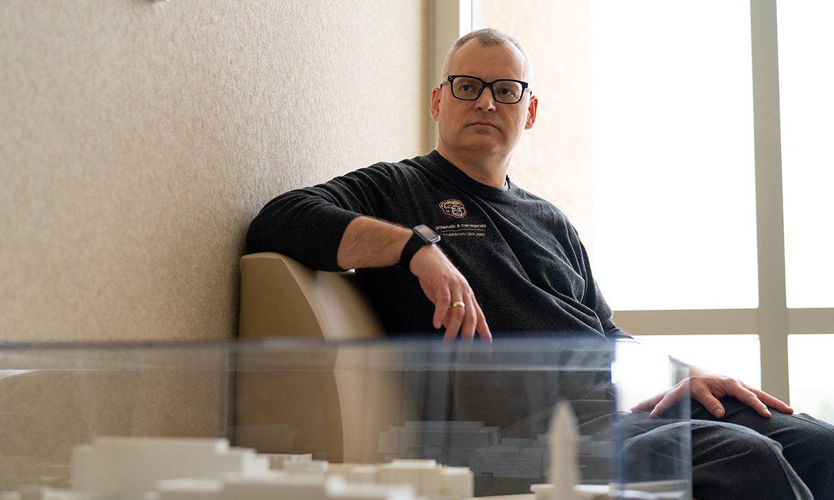 Man wearing glasses sitting in chair looking toward camera.